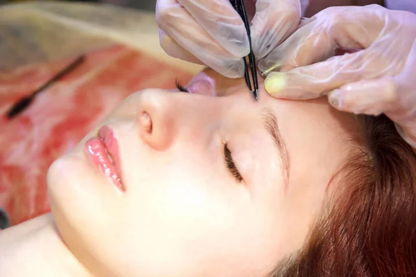 Bir güzellik salonunda bir güzellik yakın çekim cımbız ile bir müşterinin kaşları ayarlar