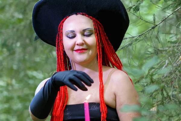 森の中で赤い髪を持つ魅惑的な魔女は、キャンドルクローズアップで愛の魔法に従事しています. — ストック写真