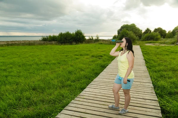 Turista mujer mirando a través de prismáticos en la plataforma de observación con vistas al lago en tiempo nublado . —  Fotos de Stock