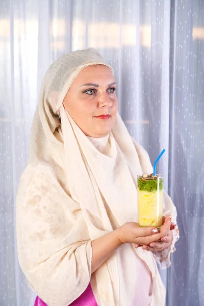 Eine junge muslimische Frau in hellem Schal hält ein Glas mit einem Frucht-Smoothie. — Stockfoto