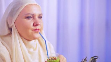 Hafif bir eşarp bir genç Müslüman kadın bir meyve smoothie içecekler ve gülümsüyor