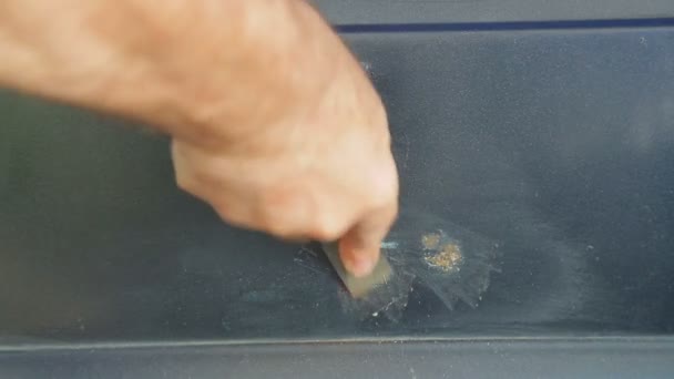 A man cleans rust on a car with a scraper — Stock Video