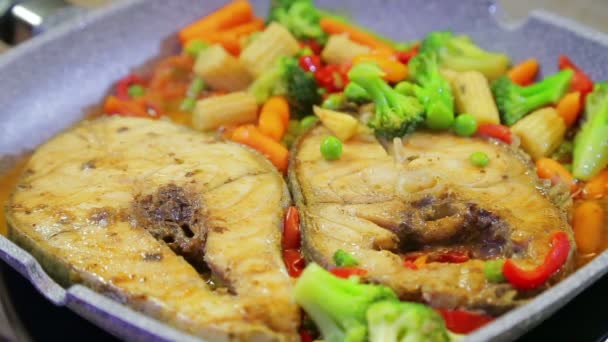 Nippers en una mano femenina revolver las verduras y el pescado en una sartén — Vídeos de Stock