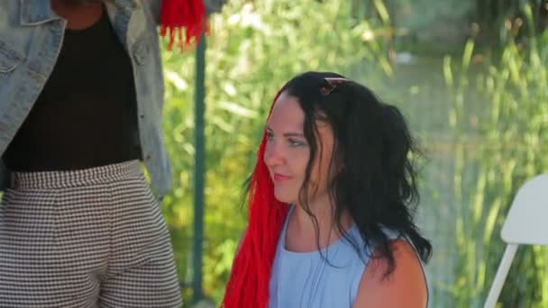 Темноволосый стилист плетет косички с красными нитками для молодой женщины — стоковое видео