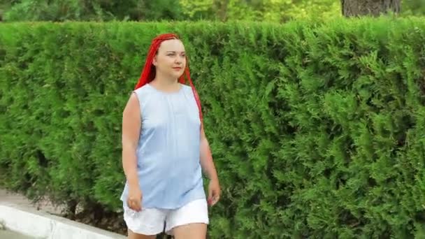 Una mujer de pelo rojo camina por los espacios verdes — Vídeos de Stock