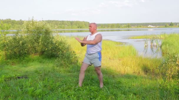 A middle aged man does breathing yoga on the lake in the morning — Stock Video