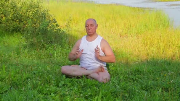 Un homme d'âge moyen fait du yoga respiratoire et médite sur le lac le matin . — Video