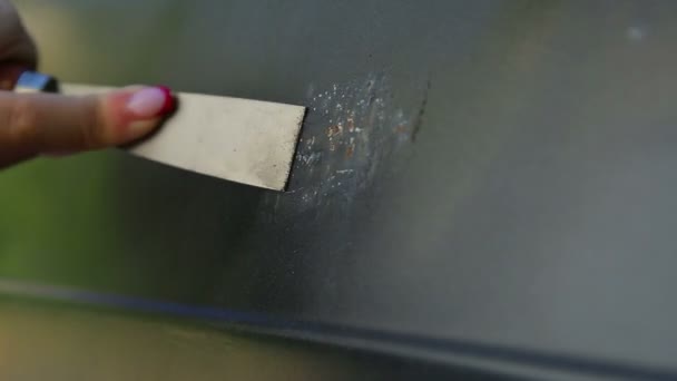 Ένα γυναικείο χέρι καθαρίζει τη σκουριά στο σώμα του αυτοκινήτου με ξύστρα. — Αρχείο Βίντεο