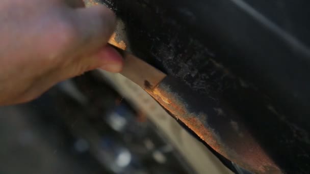 Un homme nettoie la rouille sur un corps de voiture avec un grattoir . — Video