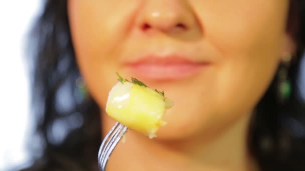 Vrouw op een witte achtergrond eet aardappelen met een vork. — Stockvideo