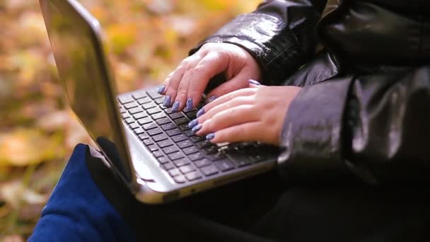 Las manos femeninas están escribiendo en un teclado de computadora sobre un fondo de hojas borrosas de otoño — Vídeo de stock
