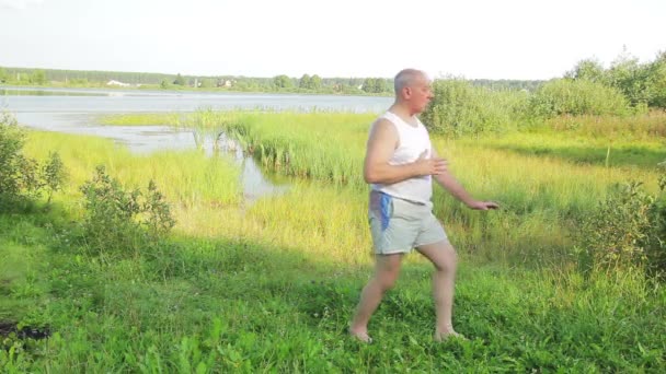 A middle aged man does yoga and breathing exercises on the lake in the morning — Stock Video