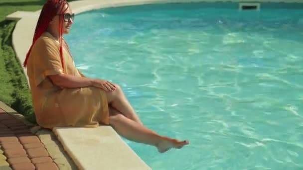 A woman dangles in the pool sitting on the edge. — Stock Video