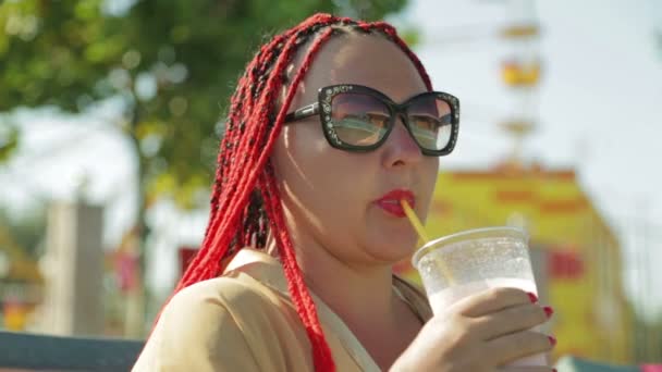 Een jonge vrouw op een ligstoel bij het zwembad drinkt een milkshake — Stockvideo