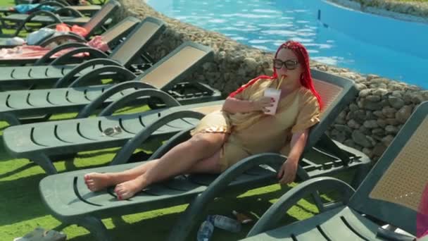 Молода жінка засмагає на стільці біля басейну . — стокове відео