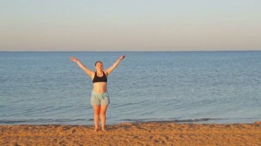 Esmer bir kadın sabahın erken saatlerinde sahilde jimnastik yapıyor..