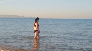 Spor mayo giymiş esmer bir kadın yoga yaptıktan sonra denizde yüzmeye gider..