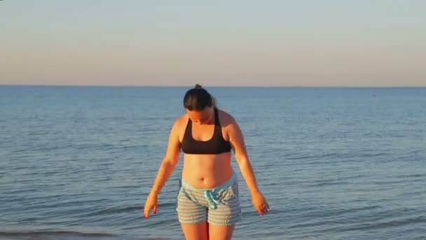 Een brunette vrouw in sportkleding doet gymnastiek aan de kust in de vroege ochtend — Stockvideo