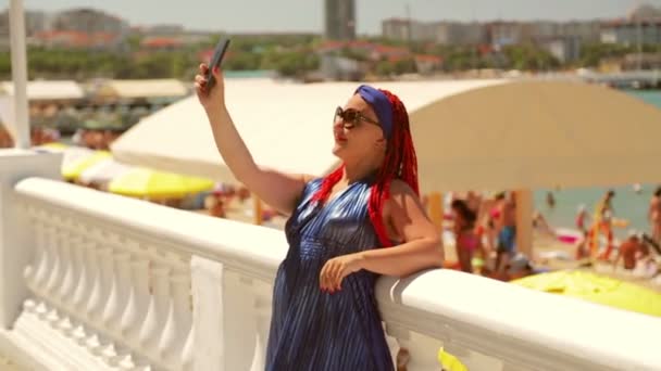 Eine junge Frau mit afrikanischen Zöpfen und Brille steht auf der Promenade und macht ein Selfie. — Stockvideo