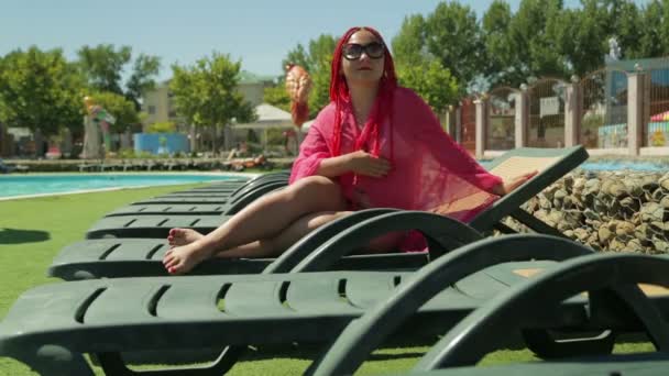 En modern judisk kvinna vid poolen i solstol njuter av solen — Stockvideo