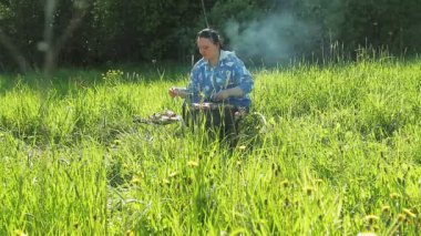 Doğada bir kadın ızgarada et ve sosis pişirir..