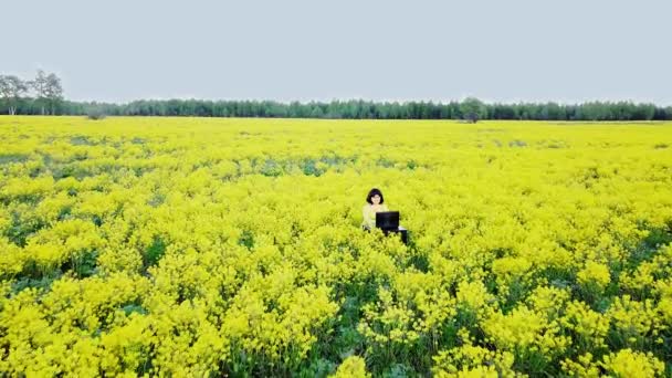 Une femme brune en vêtements jaunes au milieu d'un champ aux fleurs jaunes travaille à distance 