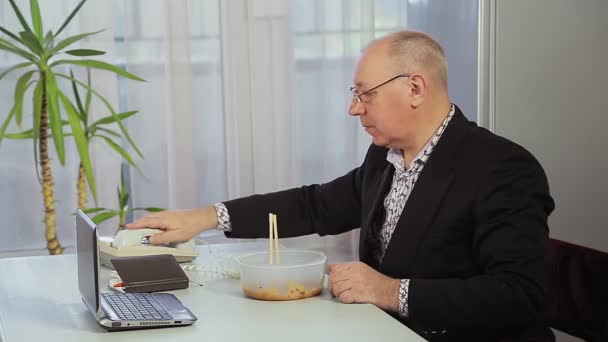 Мужчина во время обеденного перерыва обедает с помощью китайских палочек и говорит по телефону . — стоковое видео