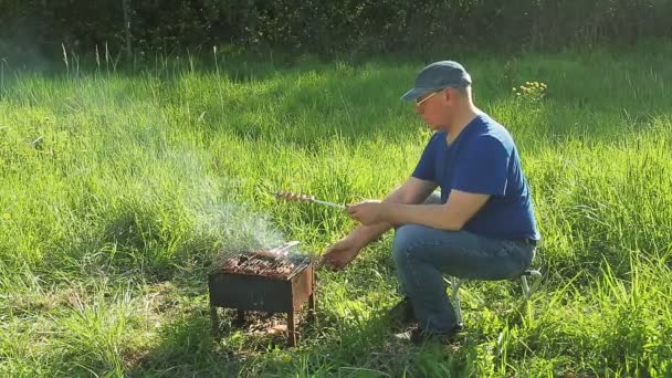 En man i naturen pommes frites på grillkött och korv. — Stockvideo