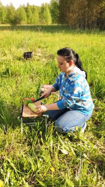 Doğadaki genç bir kadın ızgara için sebze doğruyor. Dikey