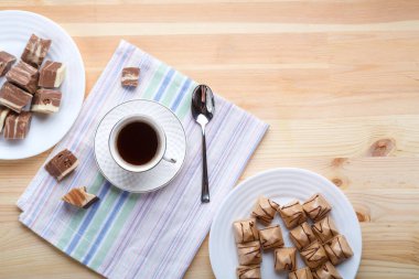 Bir fincan kahve peçetelerin üzerinde, ahşap bir masada, kruvasan ve şekerlerle..
