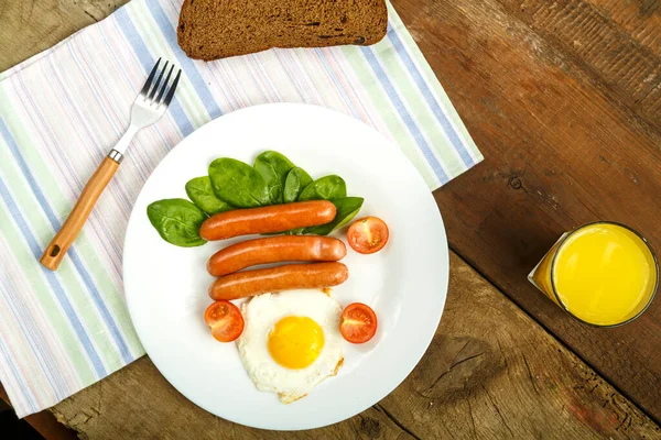 Gebratene Eier mit Würstchen und Tomaten mit Brot auf Serviette und einem Glas Saft. — Stockfoto