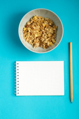Granola 'lı bir bardak ve mavi arka plana kalori yazmak için kalemli bir defter..