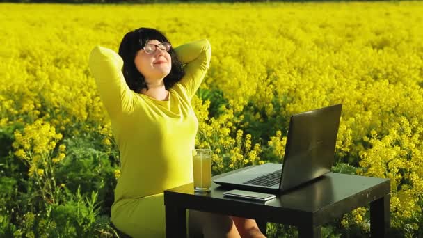 Giovane donna A in abiti gialli in un campo giallo in una giornata di sole lavora a distanza al computer . — Video Stock