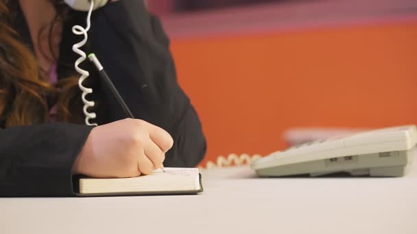 Жінка в офісі говорить по телефону і пише інформацію — стокове відео
