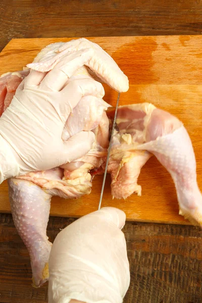 Woman cuts chicken carcass with a knife on a wooden board.