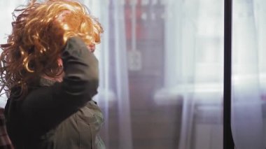 Aynanın önünde duran bir kadın altın saçlı bir karnaval peruğu takıyor..