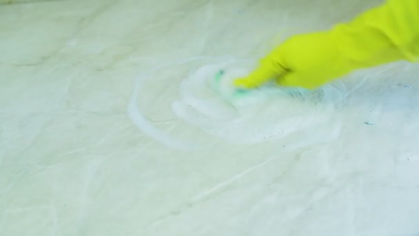 Eine Hand in einem Gummihandschuh wäscht Schmutz mit einem Schwamm mit einem Schaummittel von der Oberfläche des Tisches — Stockvideo