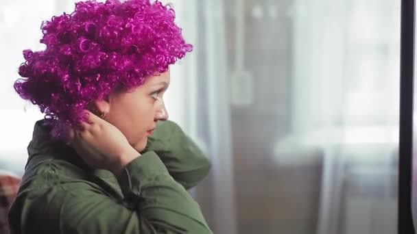 Une femme devant un miroir met une perruque de clown avec des boucles violettes . — Video