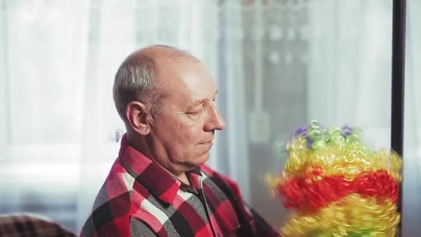 Un homme devant un miroir met une perruque de clown avec des boucles multicolores — Video