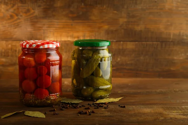 Frascos con pepinos y tomates en escabeche y especias espolvoreadas sobre una mesa de madera . —  Fotos de Stock