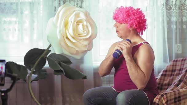 Een travestiet in een roze pruik met make-up thuis schudt halter biceps. — Stockvideo