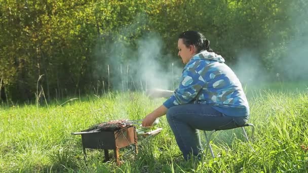 Kobieta na przyrodzie grilluje mięso i kiełbaski na grillu. — Wideo stockowe