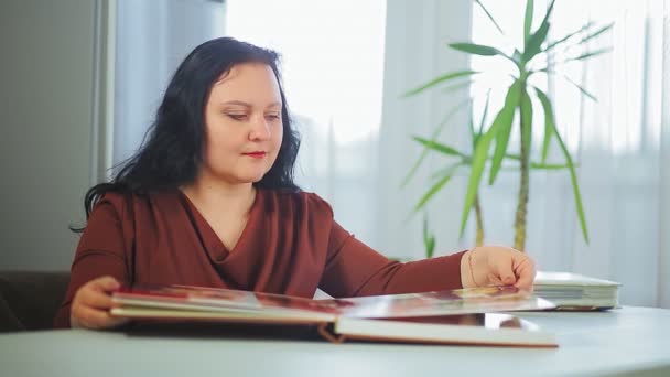 Una mujer está considerando un álbum familiar con fotos en casa — Vídeos de Stock