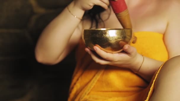 En ung kvinna i ett bad i en handduk mediterar med en sjungande skål. — Stockvideo
