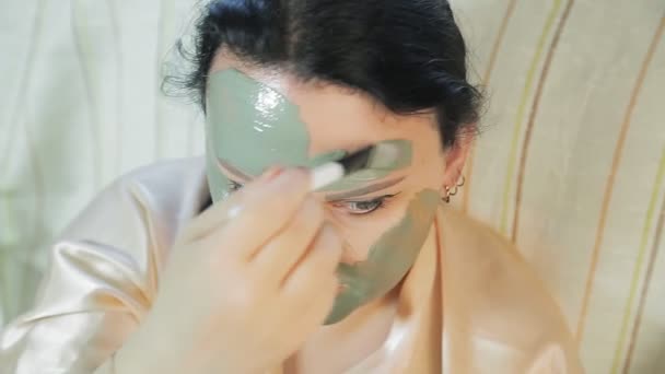 Una mujer en casa se pone una máscara de arcilla azul en la cara. . — Vídeos de Stock