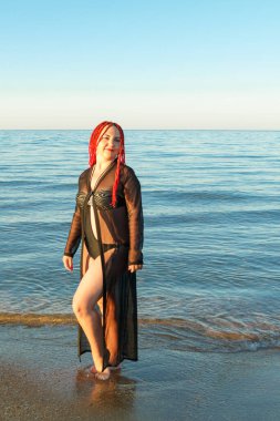 Mayolu genç bir kadın ve Afrika örgülü siyah bir hırka sahil boyunca yürüyor..