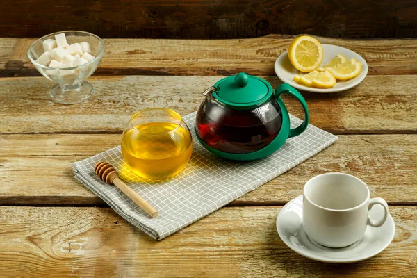 Чайник с вареным чаем и медом с лимоном и чашкой на столе . — стоковое фото