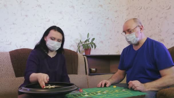 Mann und Frau in medizinischen Masken spielen Roulette zu Hause in Quarantäne in Isolation zur Vorbeugung von Coronavirus. — Stockvideo