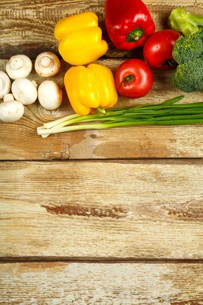 Warzywa brokułowe, cebula zielona, pomidory i papryka, grzyby wzdłuż krawędzi stołu od szorstkich desek. — Zdjęcie stockowe