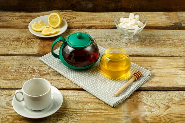 stock image Kettle with brewed tea and honey with lemon and a cup on the table.